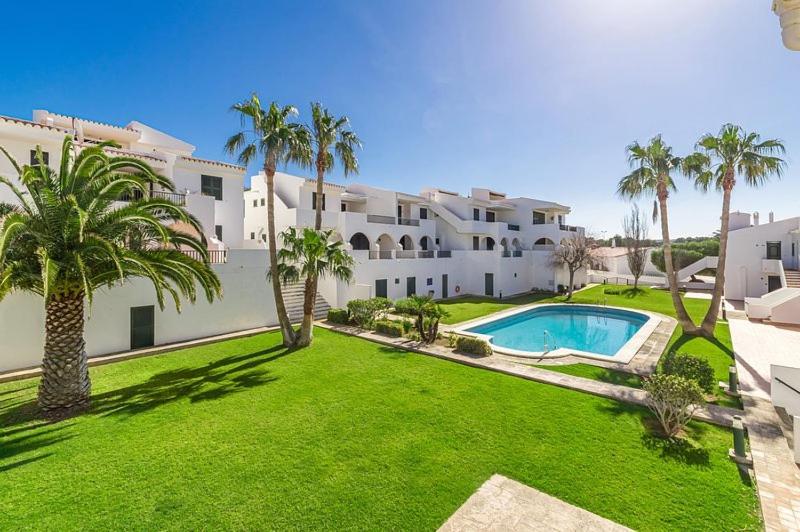 un gran edificio blanco con un patio con piscina en Apartamento Albatros-Son Parc Menorca en Son Parc