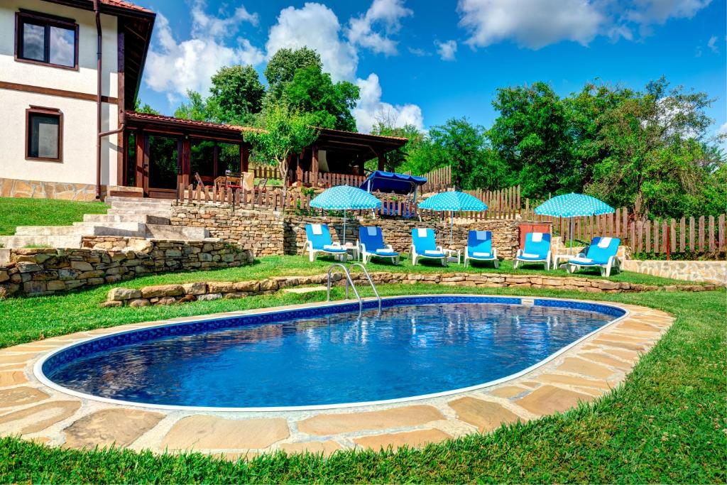 a pool in a yard with chairs and umbrellas at House Maya in Tryavna