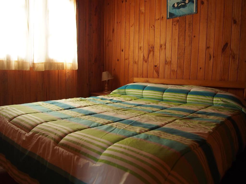 a bed in a wooden bedroom with a window at Cabañas Los Tamarugos in Pichidangui