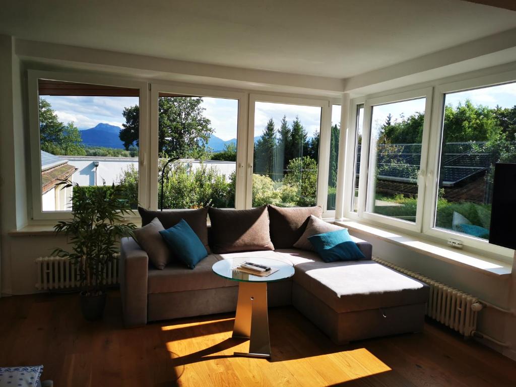 sala de estar con sofá, mesa y ventanas en Ferienwohnung Kaiserblick, en Stephanskirchen