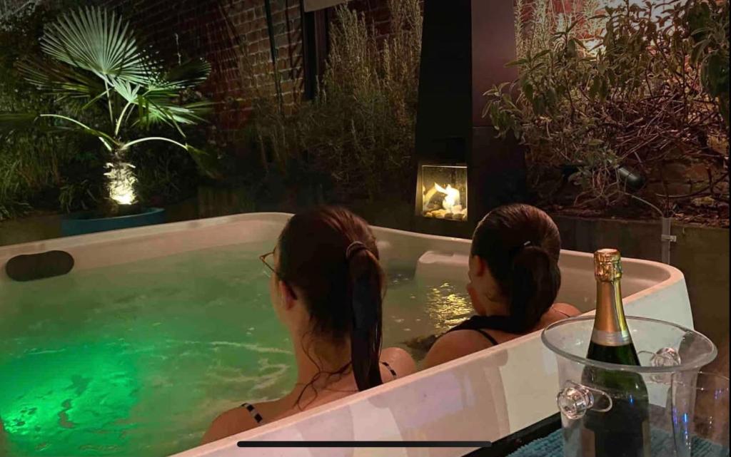 two women sitting in a bathtub with a bottle of wine at Le jacuzzi de Marie in Tourcoing