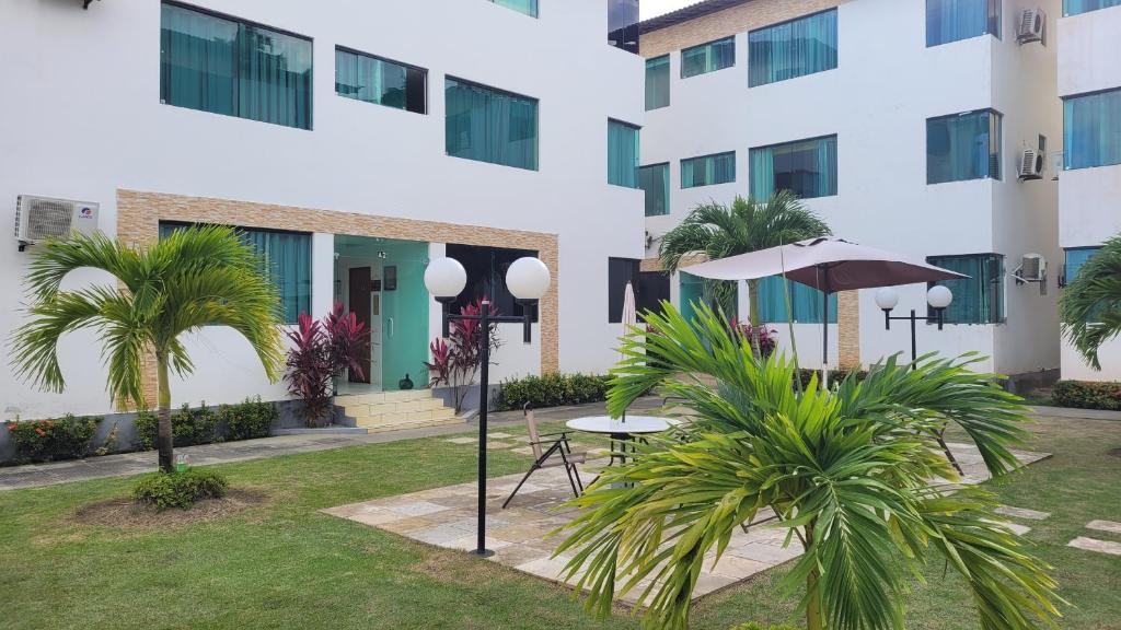 a building with a table and an umbrella and palm trees at Maragogi Flat Residence in Maragogi