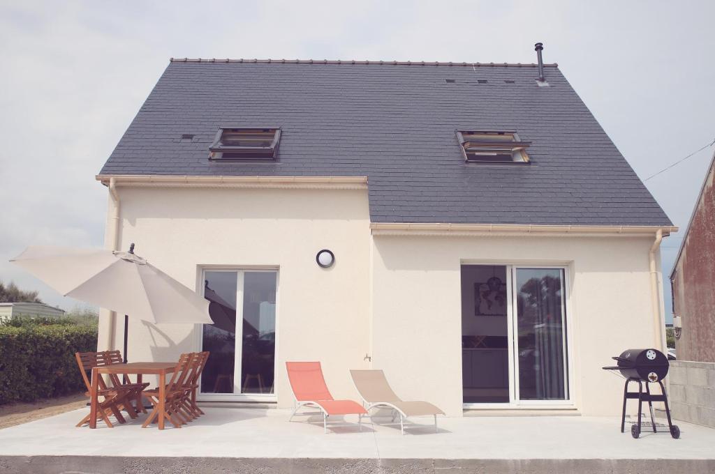 ein Haus mit Stühlen, einem Tisch und einem Sonnenschirm in der Unterkunft Maison neuve à 350m de la plage La casa Sovaïna in Cléder