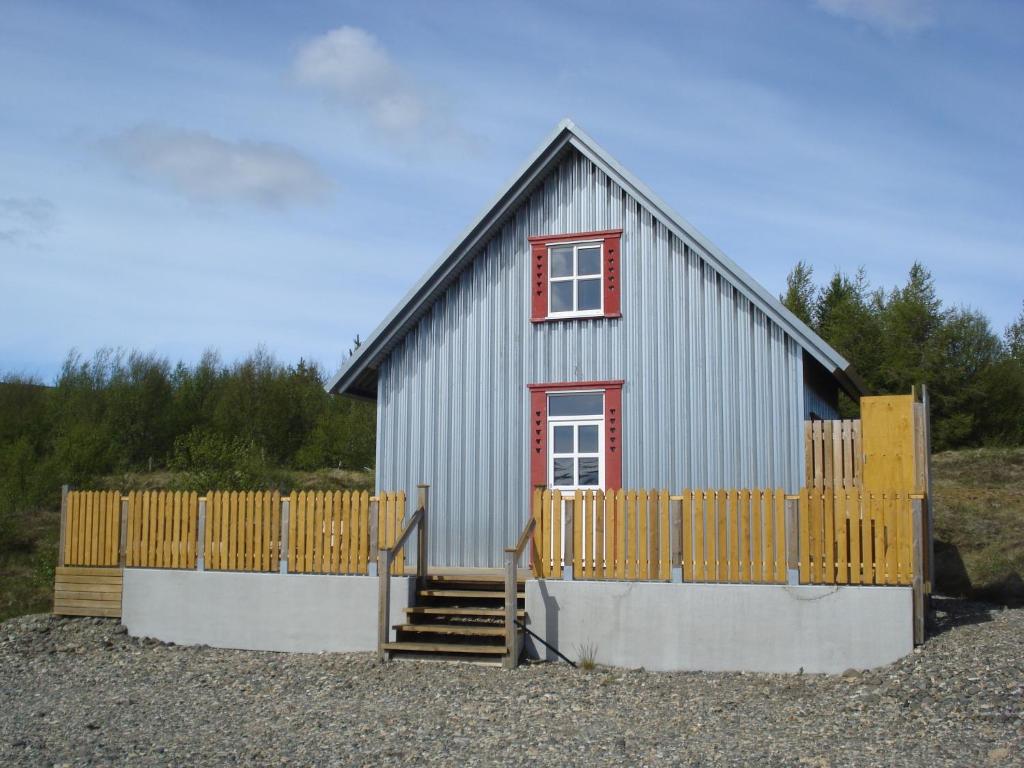 una pequeña casa gris con una ventana roja y una valla en Vinland Cottage, en Egilsstadir