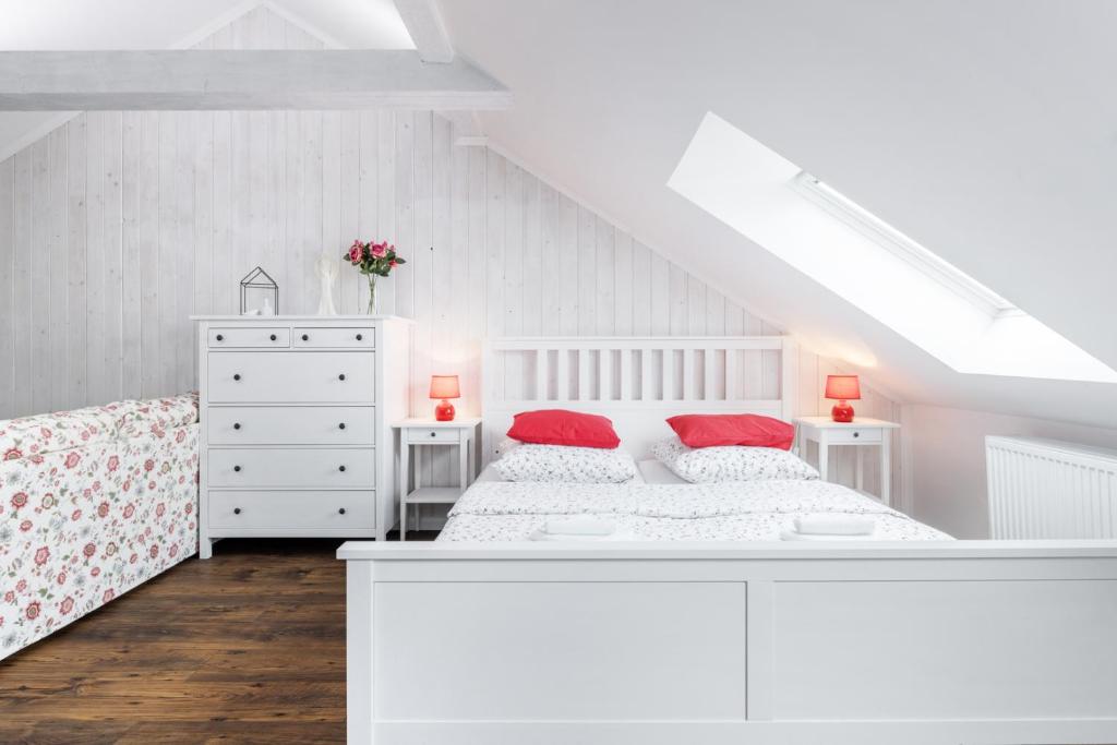 a white bedroom with a bed and two red pillows at Penzion Belle Donne in Znojmo