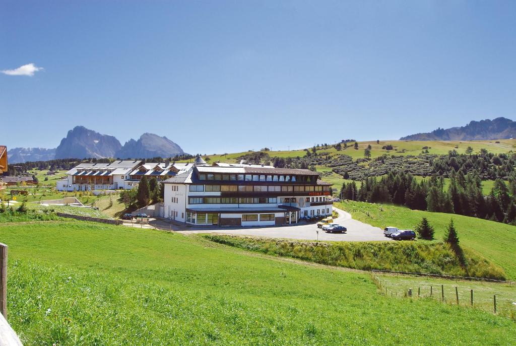 ein großes Gebäude auf einem Hügel mit einem grünen Feld in der Unterkunft Piccolo Hotel Sciliar in Alpe di Siusi