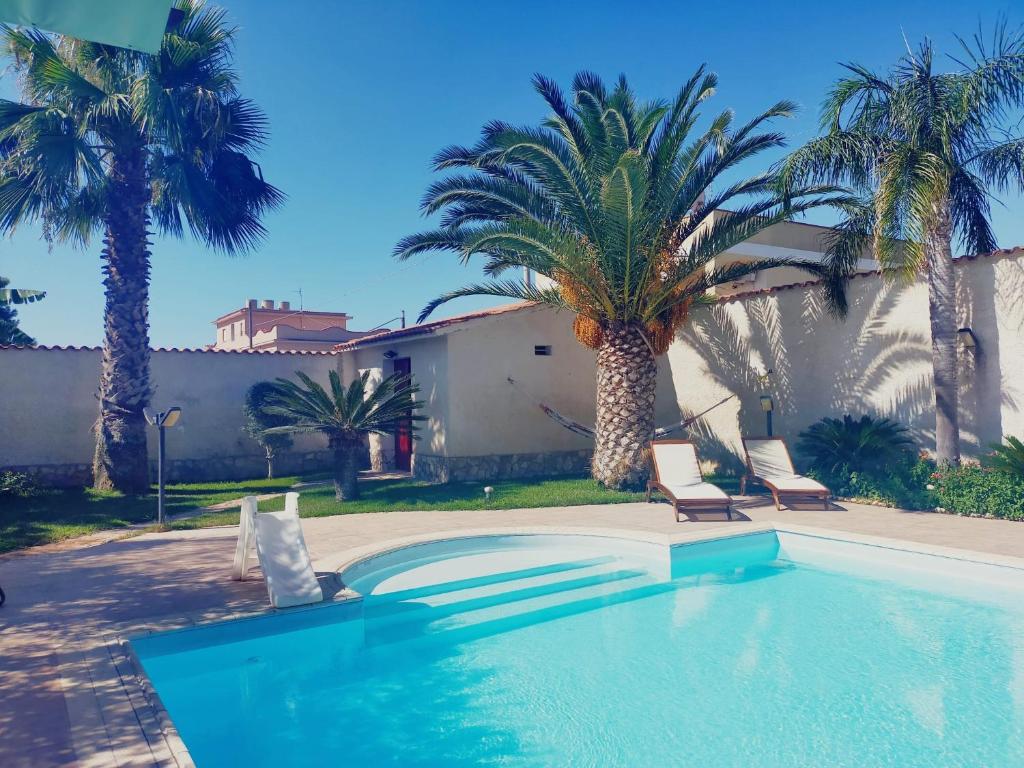 basen z 2 krzesłami i palmami w obiekcie Casa vacanza in villa con piscina! w mieście Triscina