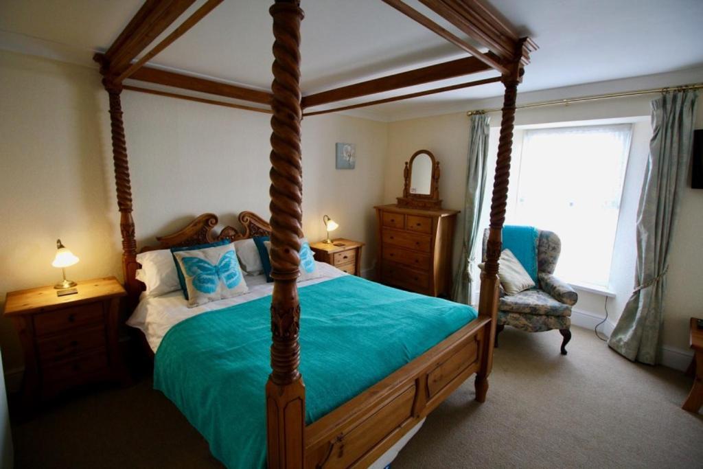 um quarto com uma cama de dossel e uma cadeira em Springwell Inn em Pendine