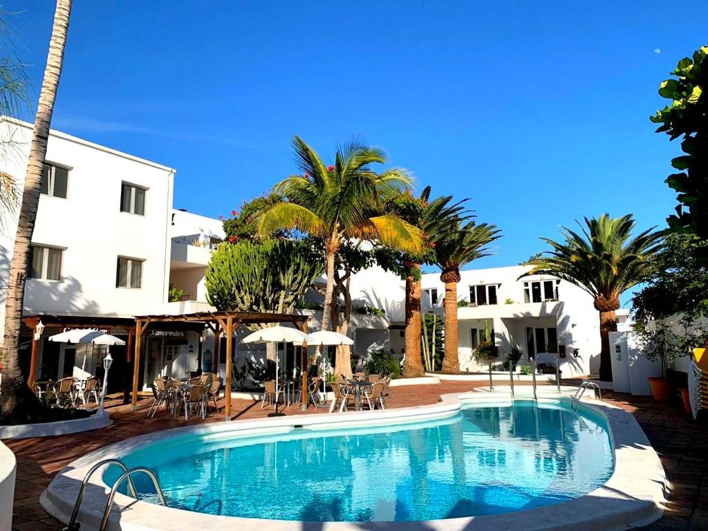 a swimming pool with palm trees and a building at Apartamentos Tamarindos in Puerto del Carmen
