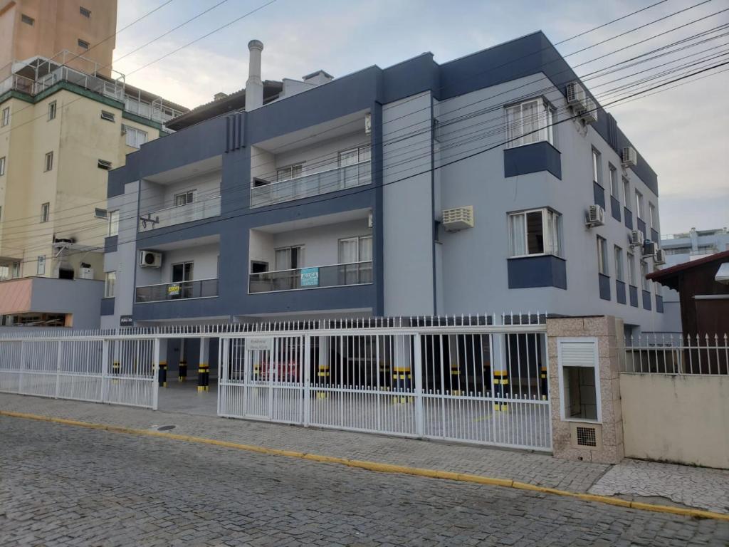 a blue building with a white fence on a street at Apto 2 quartos no centro de Bombinhas, 130 metros praia in Bombinhas