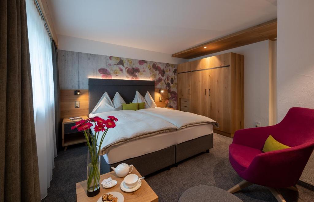 クロスタースにあるSunstar Hotel Klostersのベッドと赤い椅子が備わるホテルルームです。