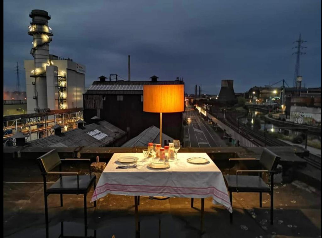 een tafel met een lamp en stoelen op een dak bij GHOSTeL 1st - Aventure Alternative - GUEST HOUSE - Arts-Factory-Experience - For artists, makers and open minds - Attention, we are not a hotel and are not adapted for everybody - Read host warnings before reservation - WWW,PROVIDENCE,BE asbl in Charleroi