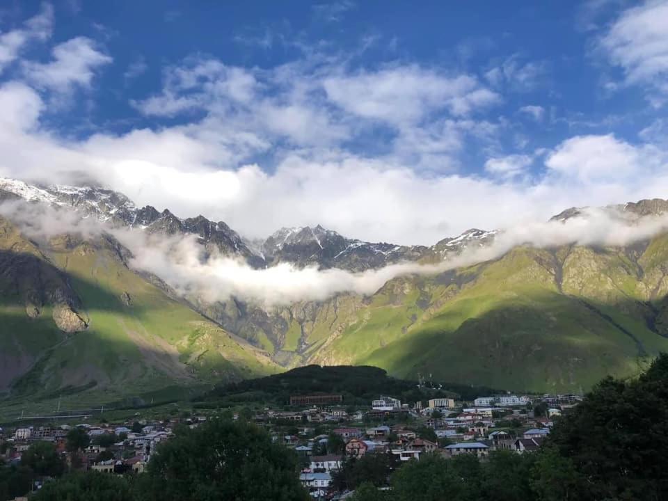 una città di fronte a una catena montuosa con nuvole di Paramount Kazbegi a Kazbegi