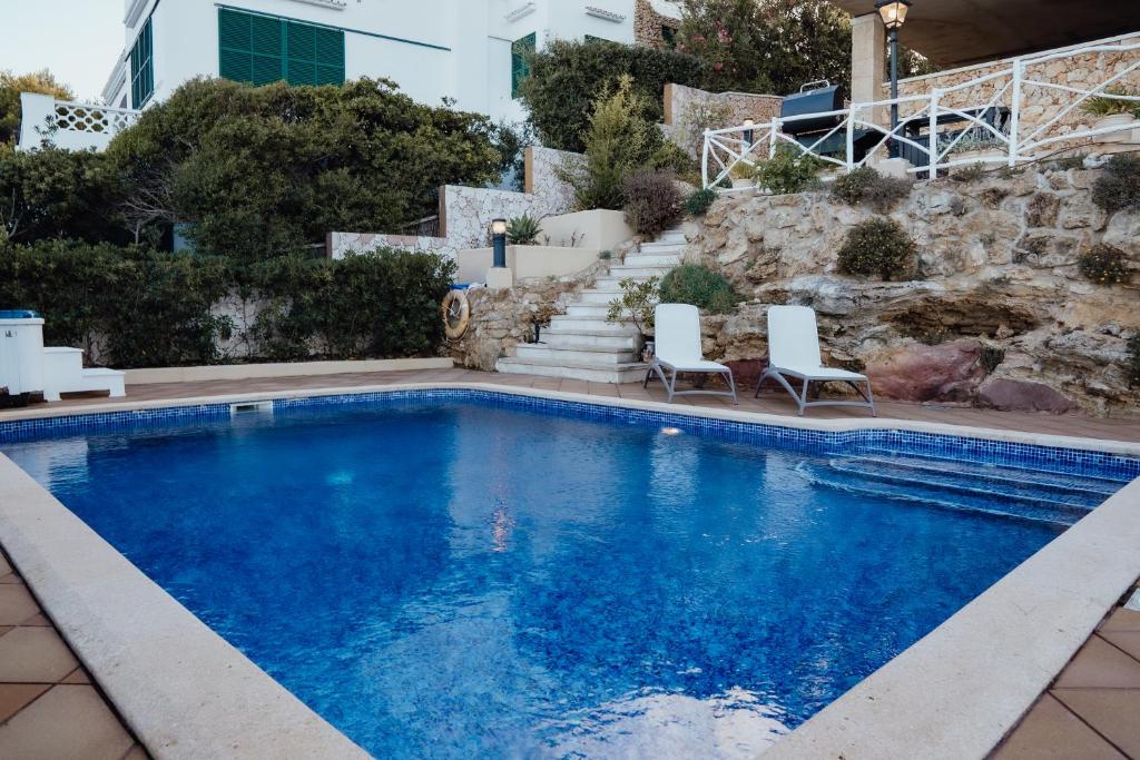 a swimming pool with two chairs and a house at Menurka - Port d'Addaia in Port d'Addaia