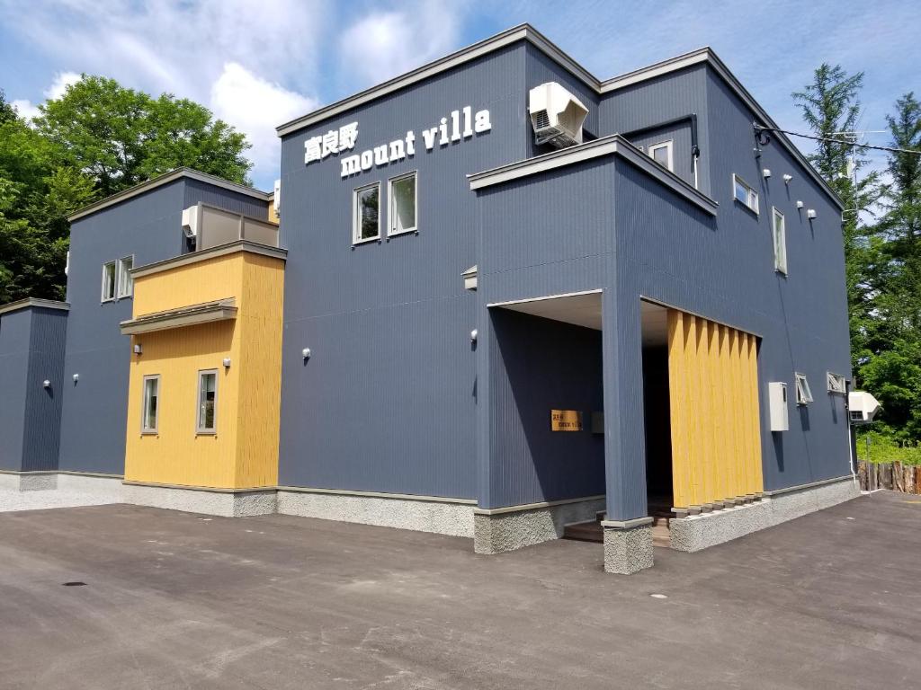 een blauw en geel gebouw met een parkeerplaats bij Furano Mount Villa in Furano