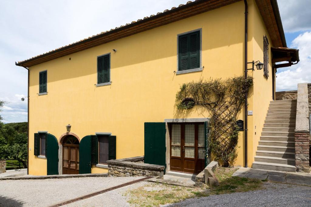 une maison jaune avec des portes vertes et un escalier dans l'établissement Casale Vacanze Il Granaio, à Cortone