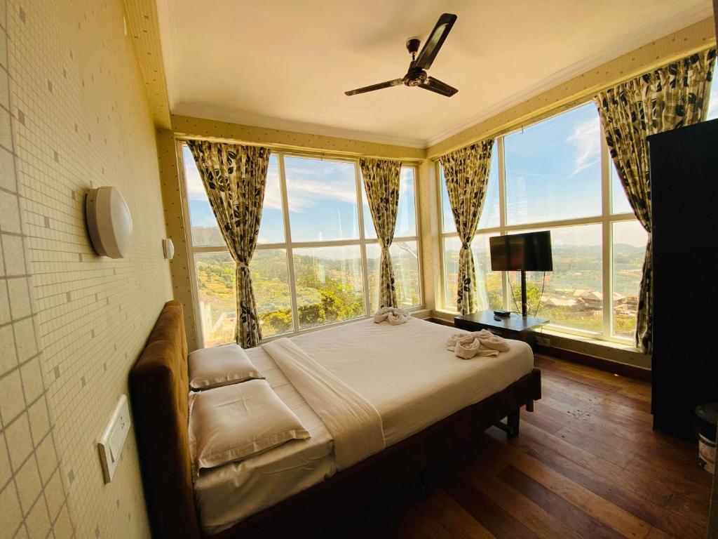 a bedroom with a bed in a room with large windows at Tulips Valley View Resorts in Ooty