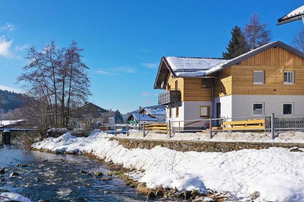 a house with snow on the ground next to a river at Ferienhaus Leutner in Bodenmais