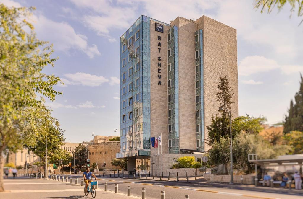 a man riding a bike in front of a tall building at Bat Sheva Jerusalem by Jacob Hotels in Jerusalem