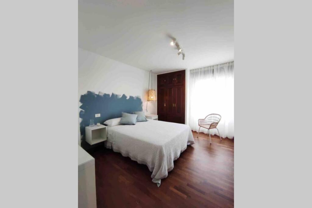 a white bedroom with a bed and a chair at Avenida 37 in Caldas de Reis