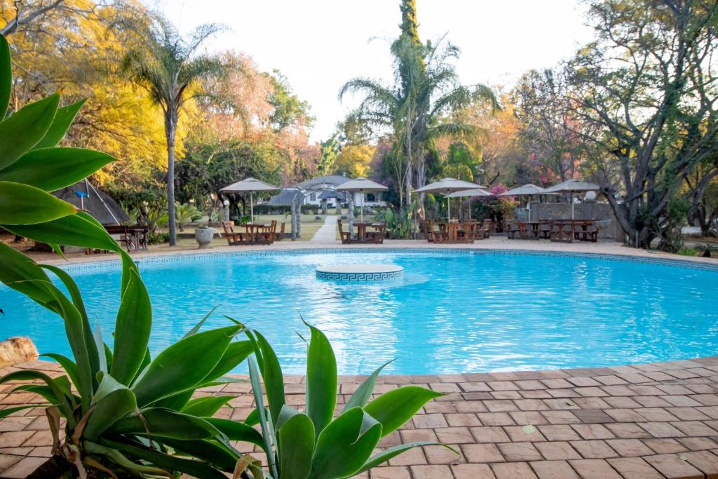 a large swimming pool with tables and umbrellas at BON Hotel Rustenburg in Rustenburg