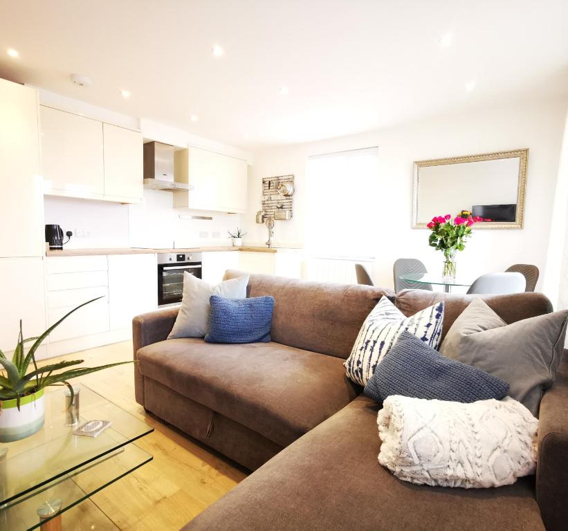 a living room with a brown couch and a kitchen at Apartment in the heart of East Wittering Village in Chichester