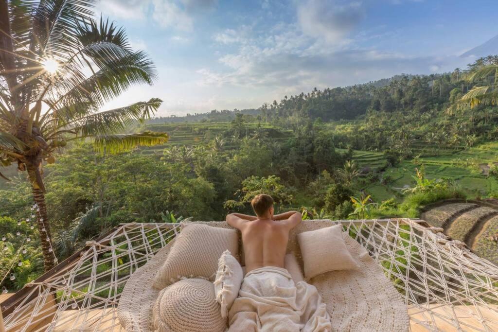 a man laying on a hammock looking out over a valley at Camaya Bali - Magical Bamboo Houses in Selat
