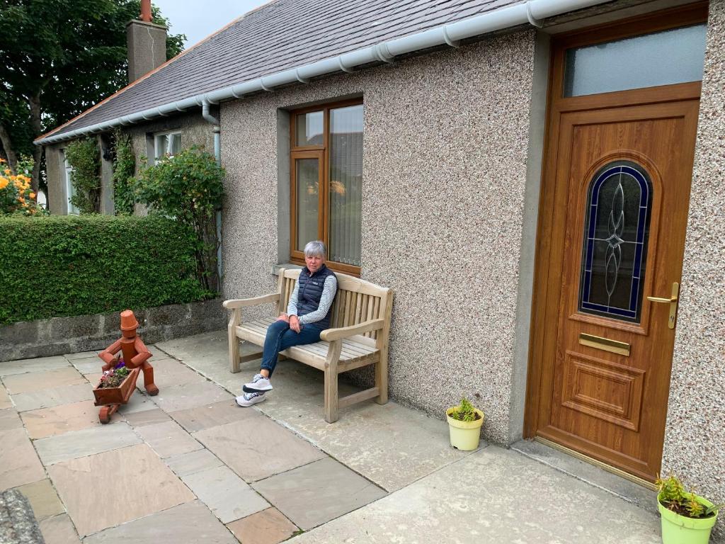 un hombre sentado en un banco frente a una casa en 8 Thoms Street en Kirkwall