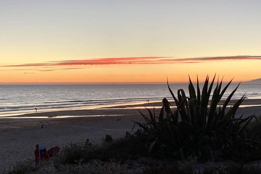 - un coucher de soleil sur la plage avec des personnes se promenant sur la plage dans l'établissement Aroeira - Sea & Golf Apartment, à Aroeira