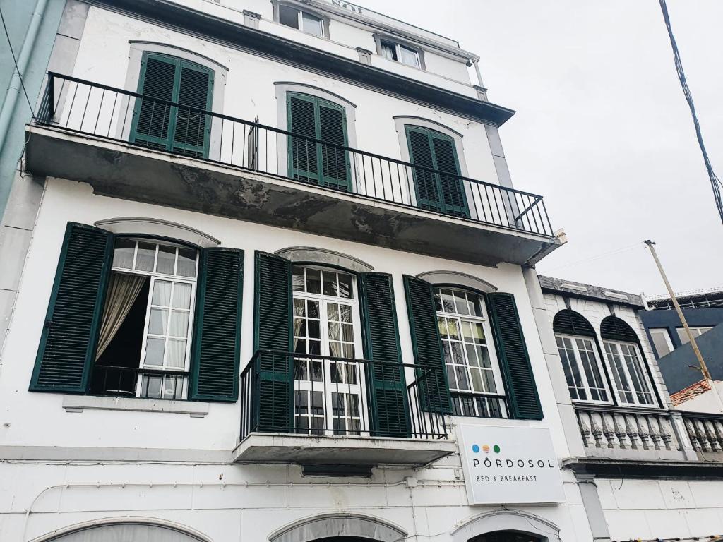 フンシャルにあるHospedaria Pôr do Solの緑のシャッター付き窓がある白い高い建物