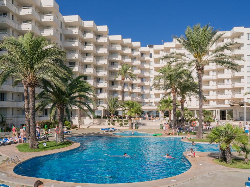 un complexe avec une piscine et des palmiers dans l'établissement Aparthotel Playa Dorada, à Sa Coma