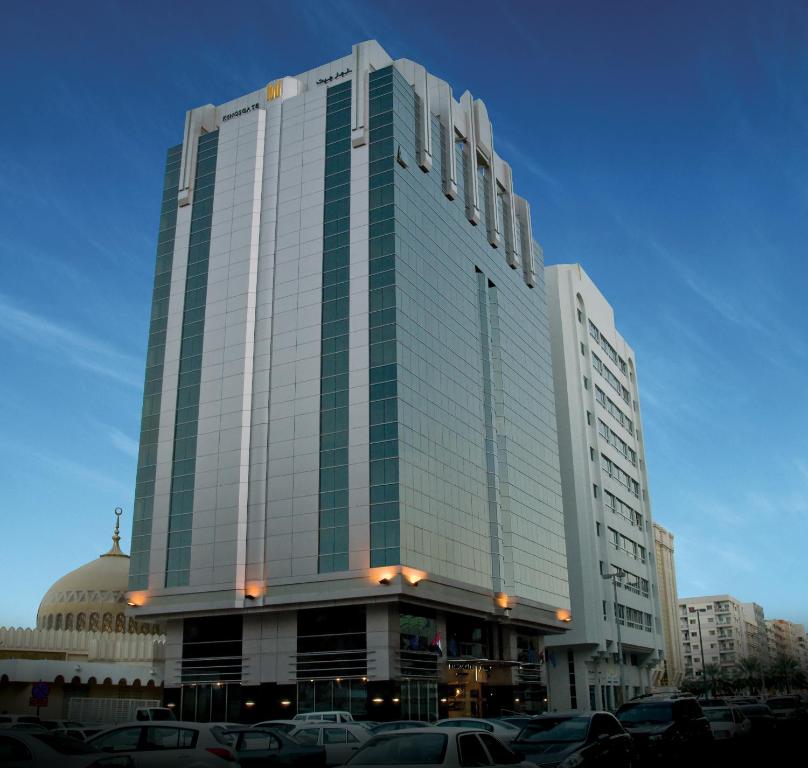 Kingsgate Hotel by Millennium في أبوظبي: مبنى طويل وبه سيارات متوقفة في موقف للسيارات