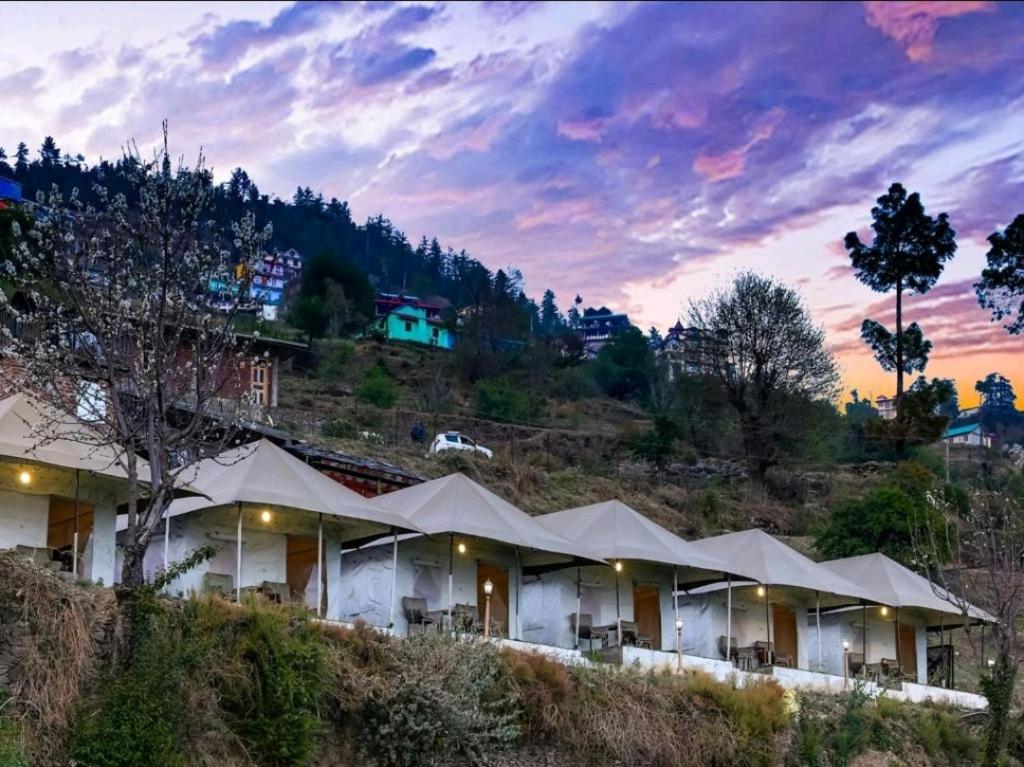 a building with white umbrellas on a hill at Dawn N Dusk Glamping tents with quintessential valley view in Chail