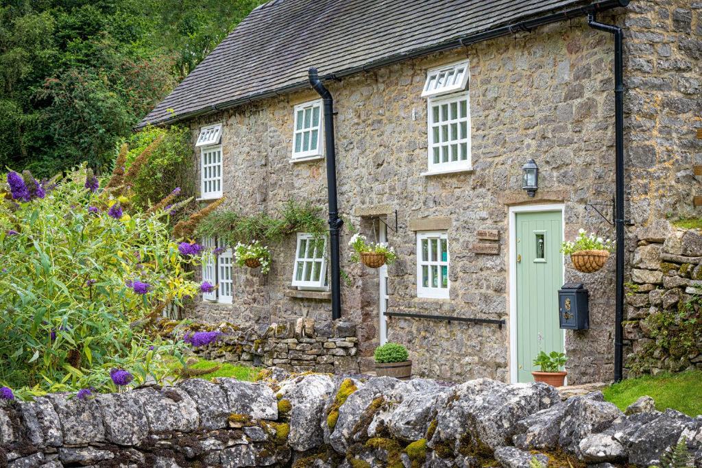 a stone cottage with a green door and a stone wall at Bankside Cottage in Alstonfield