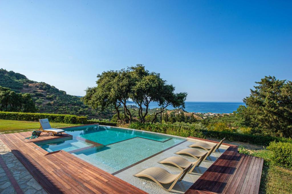 a swimming pool with chairs and the ocean in the background at Wild Oak Estate - Stone Villa with Sea Views , by ZanteWize in Argassi