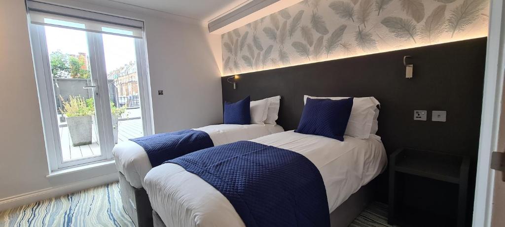 two beds in a hotel room with a window at Commodore Hotel in London