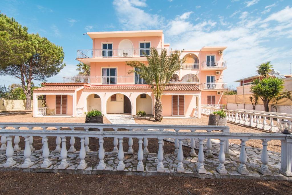 duży różowy dom z białym płotem w obiekcie Southgate Apartments w mieście Agios Georgios