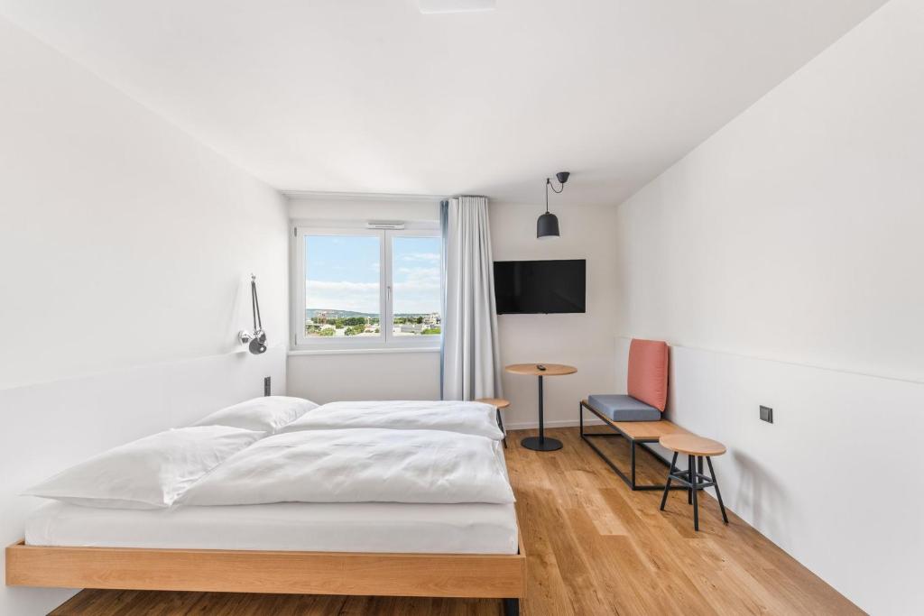 a white bedroom with a bed and a table at SMARTments business Wien Heiligenstadt in Vienna