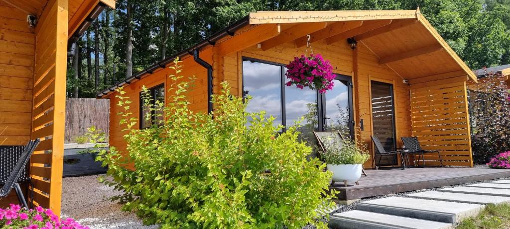 a small wooden cabin with a deck and flowers at Kantadaj Village Domki Prestige in Prudnik