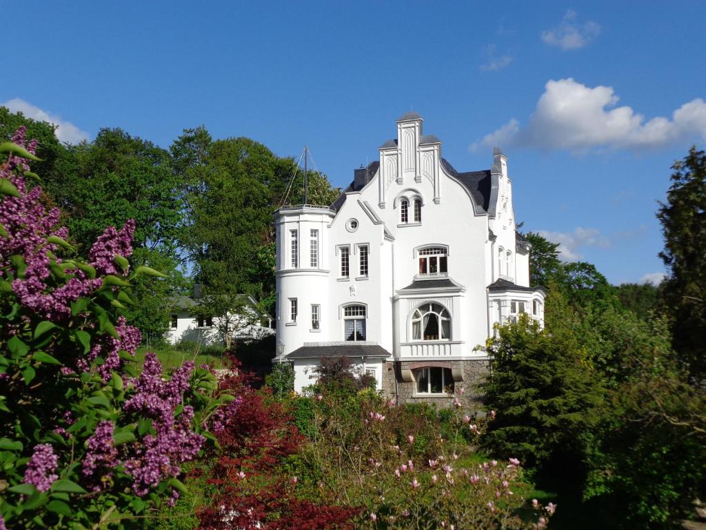 a white house surrounded by trees and flowers at WeisseVilla Friedrichsbrunn Fewo SOLIDE in Thale