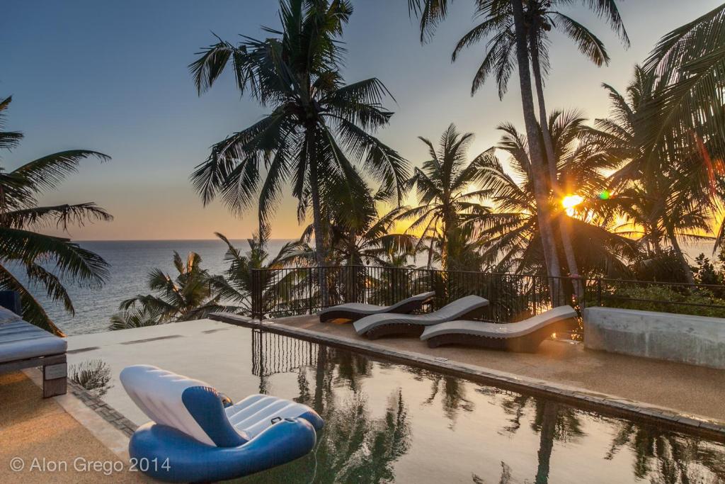 uma piscina com duas cadeiras azuis e brancas junto ao oceano em Nisala Villas em Mirissa