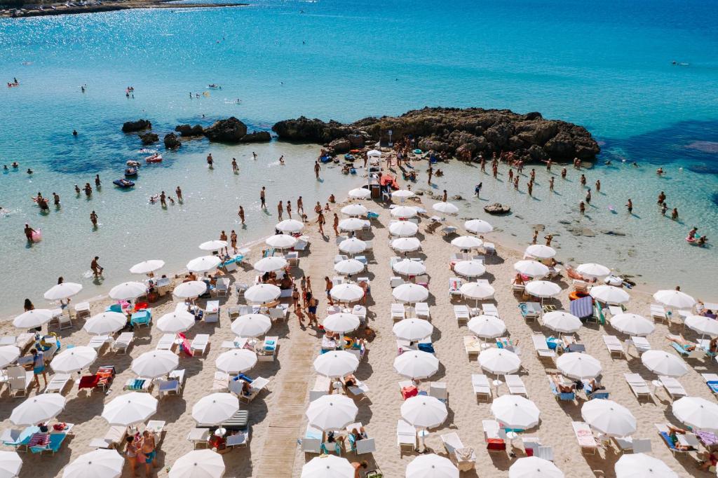 een groep mensen op een strand met parasols bij Nicolaus Prime Il Gabbiano Hotel in Pulsano