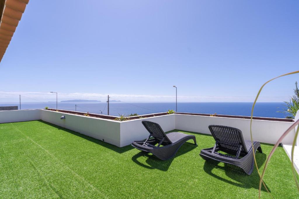 a balcony with two chairs on the grass at Flowers island house 3 in Caniço