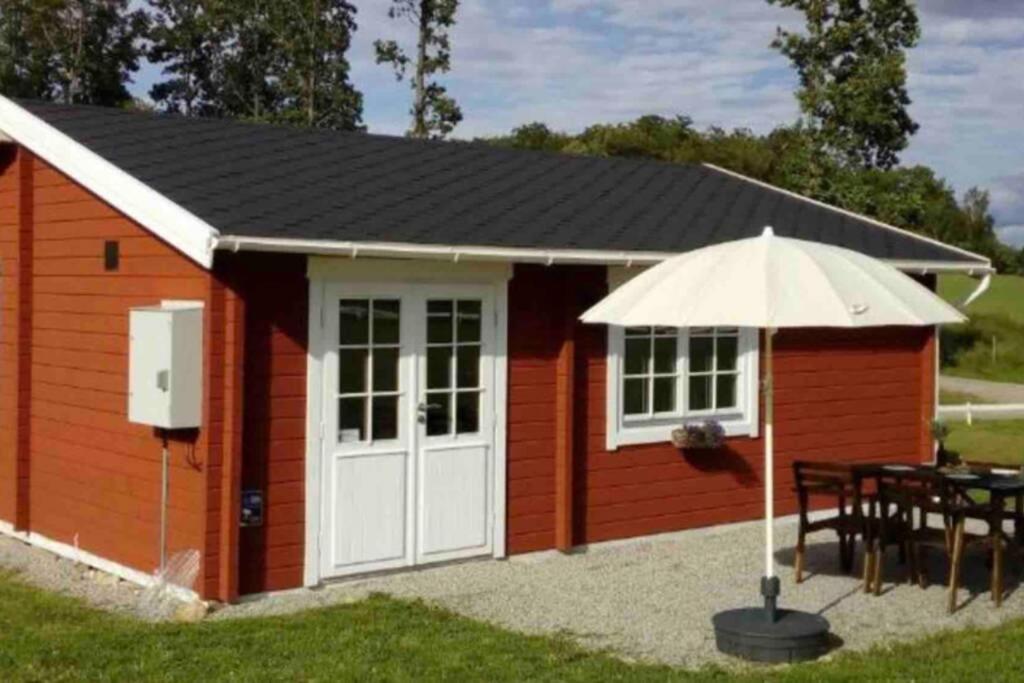 a red shed with a table and an umbrella at Cozy Cottage near lake in Hässleholm