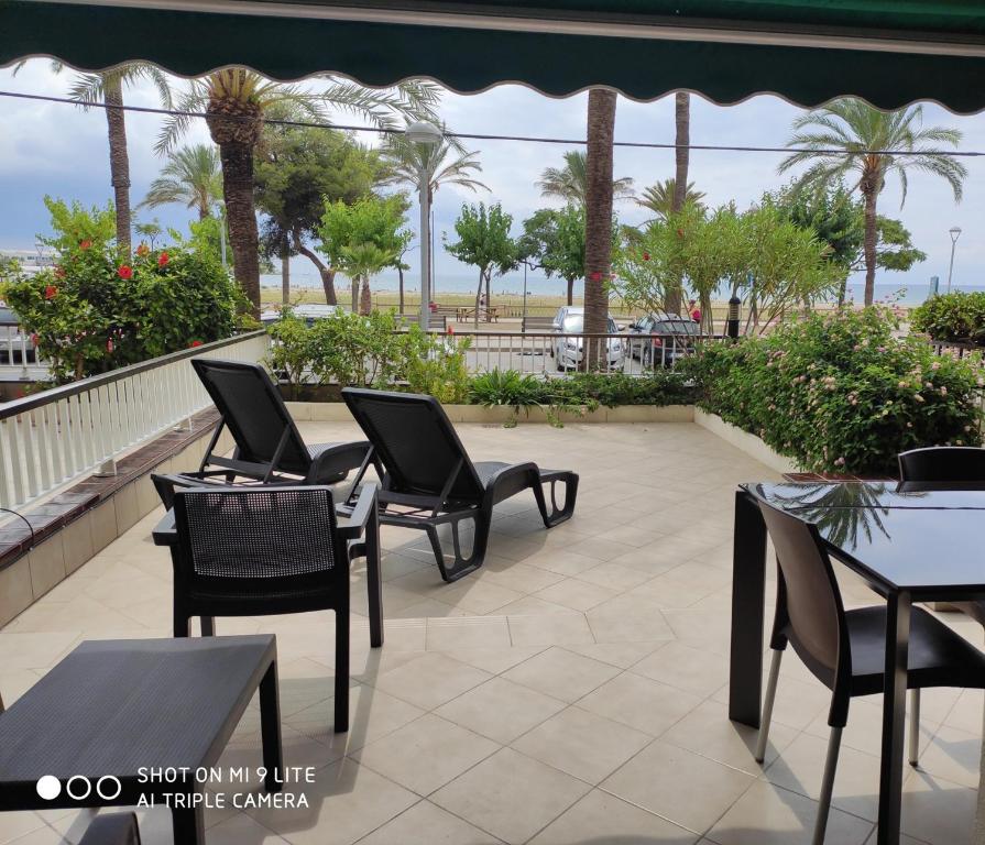 un patio con mesas, sillas y palmeras en vilanova-beach en Vilanova i la Geltrú