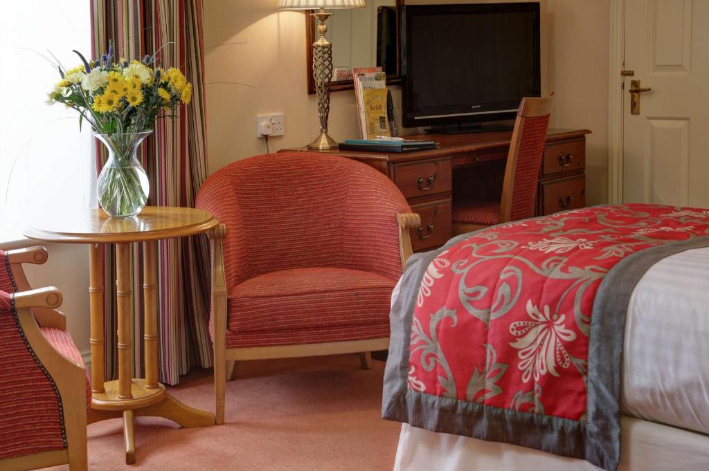 a bedroom with a bed and a vase of flowers on a table at Old Hunstanton Le Strange Arms Hotel in Hunstanton