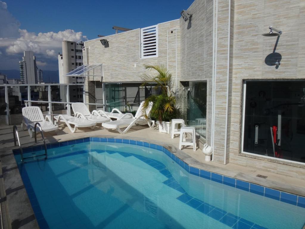 a swimming pool with white chairs and a building at Gonzaga Flat in Santos