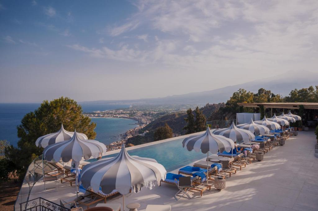 eine Reihe von Sonnenschirmen und Stühlen neben einem Pool in der Unterkunft San Domenico Palace, Taormina, A Four Seasons Hotel in Taormina