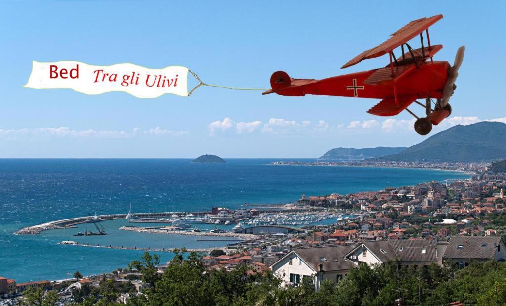 een klein rood vliegtuig dat over een stad vliegt bij Tra Gli Ulivi in Pietra Ligure