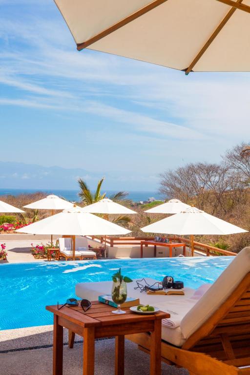 Swimming pool with white umbrellas, loungers, and ocean view in background.